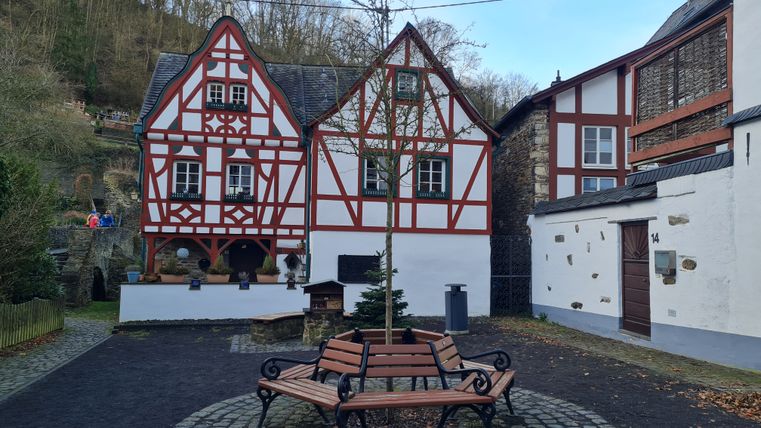 Fachwerkhäuser mit rotem Holzrahmen und einem Baum in der Mitte eines gepflasterten Platzes.