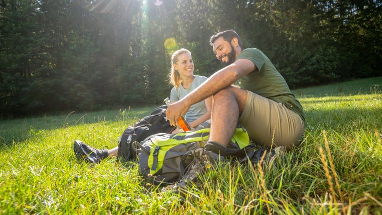 Two people are sitting in a meadow in the forest, taking a break from hiking.