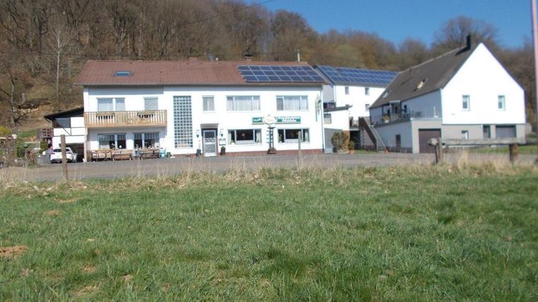 Een charmant gebouw in een landelijke omgeving met een groene grasmat. Op de voorgrond zijn weiden te zien, en op de achtergrond staan bomen.