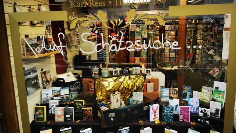 A display window of a bookstore with many different books and a treasure chest. The window decoration includes the inscription "On a treasure hunt ...".