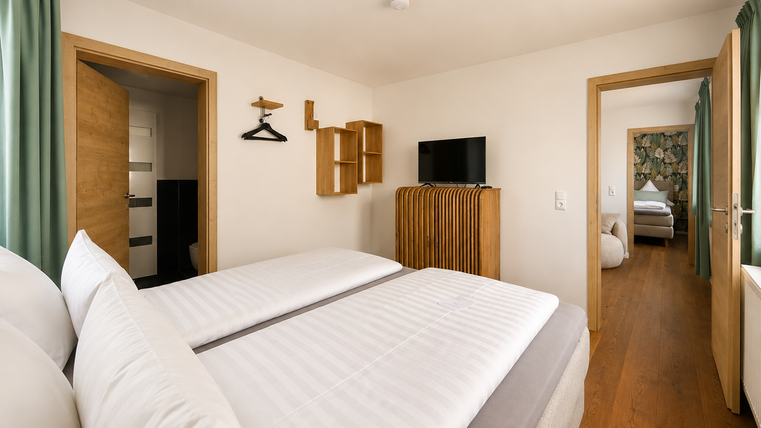 Een modern slaapkamer met twee bedden en zachte kleuren. Op de achtergrond is een andere ruimte zichtbaar.
