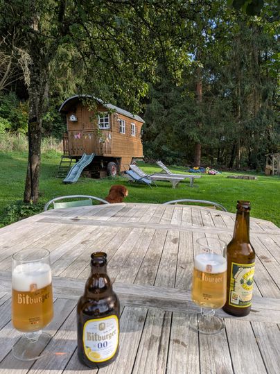 Ein Tisch im Freien mit drei Bierflaschen und Gläsern. Im Hintergrund steht ein Holzhaus und es gibt Liegen auf dem Rasen.