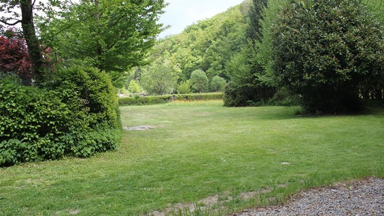 Een groene weide omringd door bomen en struiken. Op de achtergrond zijn zachte heuvels te zien.