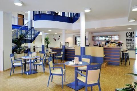 Un café moderne avec des meubles bleus et blancs. Il y a des tables, des chaises et un comptoir en arrière-plan.