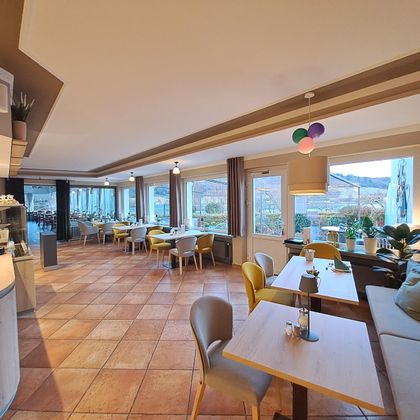 A modern restaurant with bright windows and colorful chairs. The space is designed to be friendly and inviting.