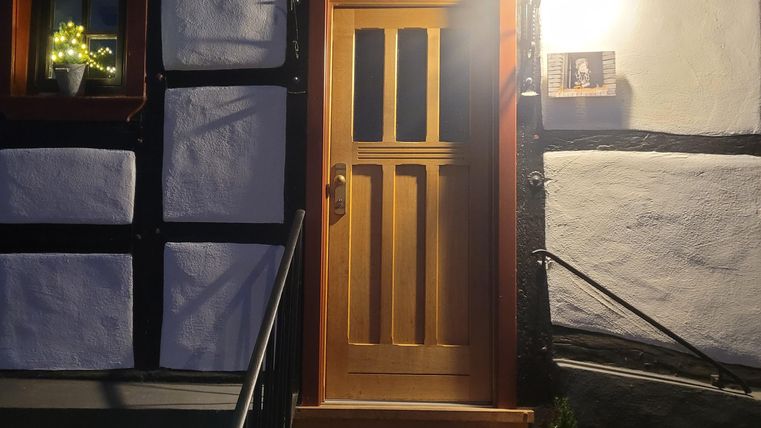 Eine einladende Haustür aus Holz mit Glasdach, umgeben von einer Treppe und einem kleinen Garten. Es ist spät am Abend und die Beleuchtung sorgt für eine warme Atmosphäre.