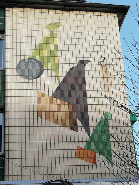 A mural with geometric shapes in various colors. The design includes green, brown, and gray elements on a light background.