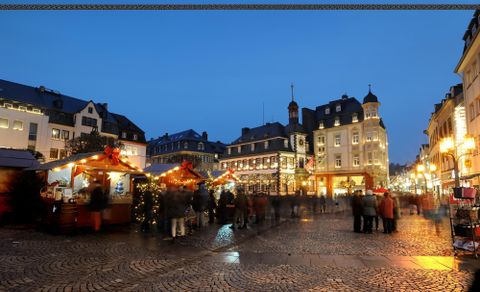 Een feestelijke marktplaats bij schemering met feestelijk versierde stands. Mensen slenteren door de pittoreske omgeving.