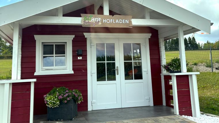 Een rood houten huis met een wit dak en een uitnodigende voordeur. Voor het huis staan planten in potten en het gebied is onderhouden.