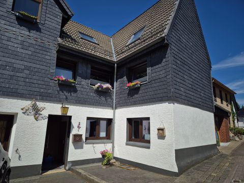 Ein charmantes Fachwerkhaus mit einem schwarz-weißen Anstrich. Blumenkästen schmücken die Fenster und der Himmel ist klar und blau.