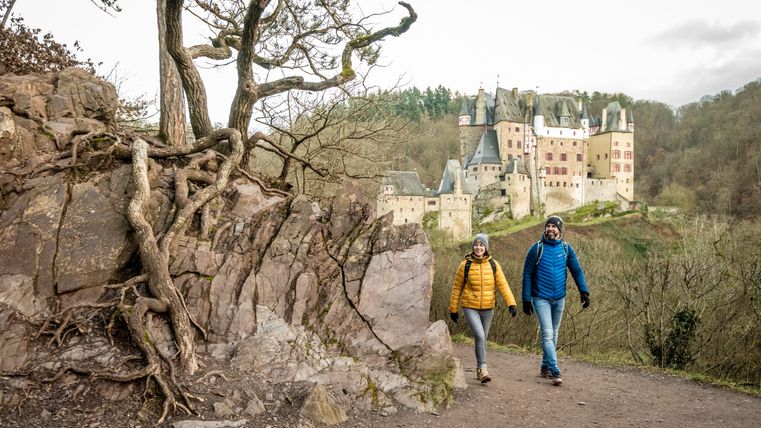 Twee wandelaars op een pad met kasteel Eltz op de achtergrond.