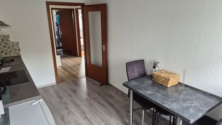 Een moderne keuken met een eettafel en stoelen. Op de achtergrond is een open kamer te zien.
