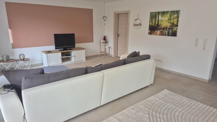 Un salon moderne avec un canapé blanc confortable et une télévision. Une image d'un paysage forestier est accrochée au mur.