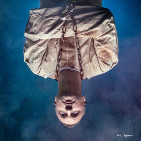 Een man in een witte gevangeniskleding, die met ketens is gebonden. De achtergrond toont een mysterieuze, mistige sfeer.