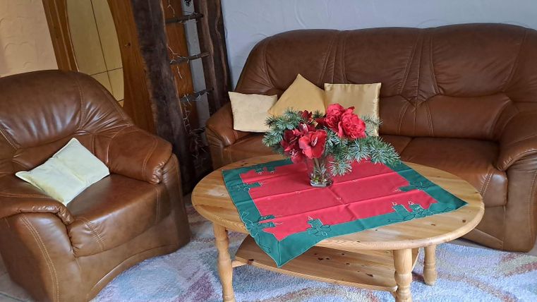 A living room with a brown leather couch and an armchair. On the table lies a red placemat with a floral arrangement.