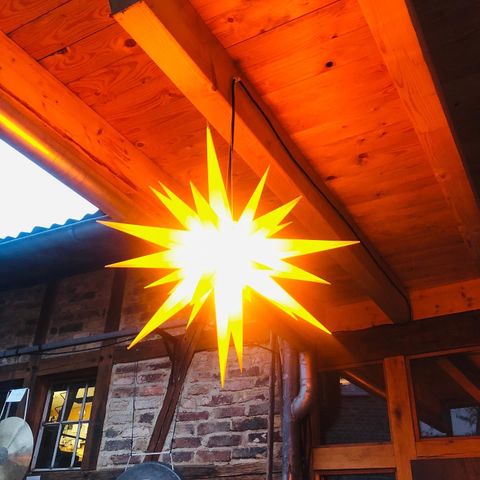 Eine leuchtende Sternenlampe hängt unter einer Holzdecke. Das warme Licht strahlt eine gemütliche Atmosphäre aus.