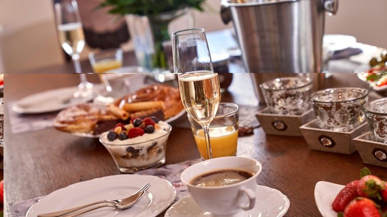 Ein schön gedeckter Tisch mit verschiedenen Frühstücksleckereien. Es gibt Sekt, frisches Obst und eine Tasse Kaffee.