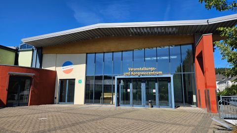 Ein modernes Veranstaltungs- und Kongresszentrum mit großen Fenstern. Die Fassade ist in verschiedenen Farben gestaltet und der Eingang ist einladend.