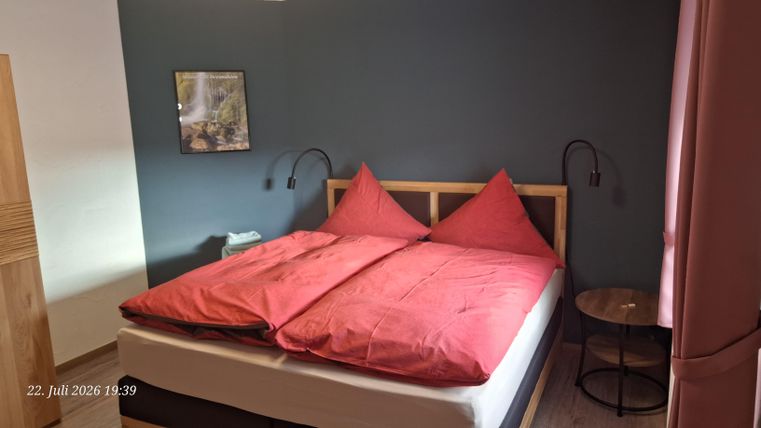 A cozy bedroom with a large bed and red pillows.
On the wall hangs a picture, and there is a small table beside it.