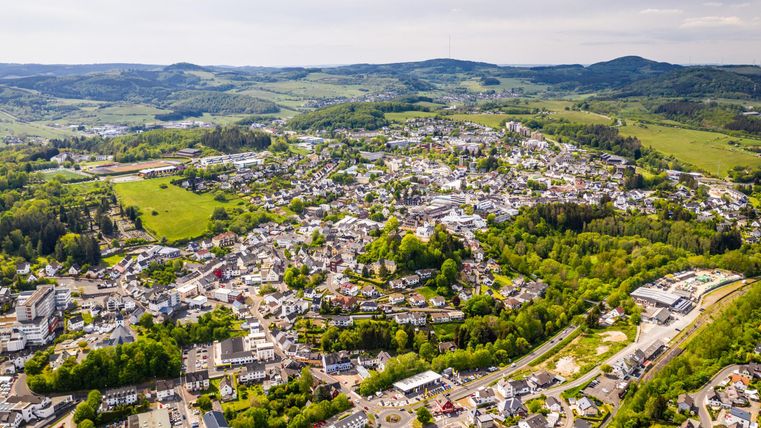 Een luchtige kijk op een kleine stad omgeven door groene heuvels en bossen. De stad heeft talrijke gebouwen en straten die harmonieus in het landschap passen.