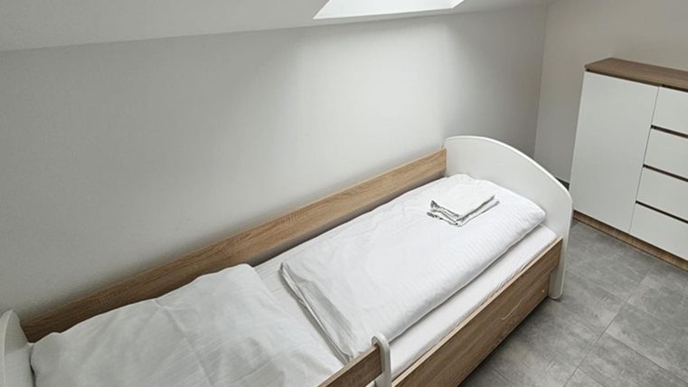 Une chambre simple avec un lit simple et une armoire. Elle a un look lumineux et moderne et un velux.