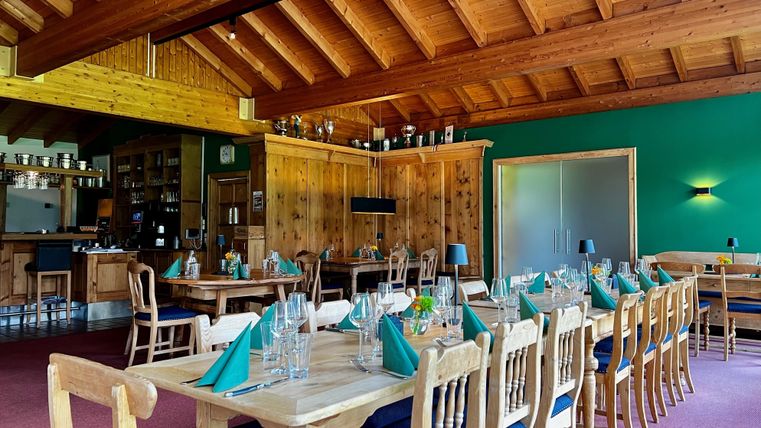 Rustic restaurant with wooden furniture, set tables, and green napkins. Wooden ceiling and green walls create a cozy atmosphere.