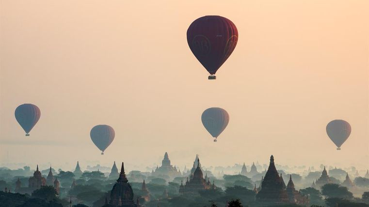 Heißluftballons steigen über eine neblige Landschaft mit Tempeln. Die sanften Farbverläufe des Himmels schaffen eine ruhige Atmosphäre.