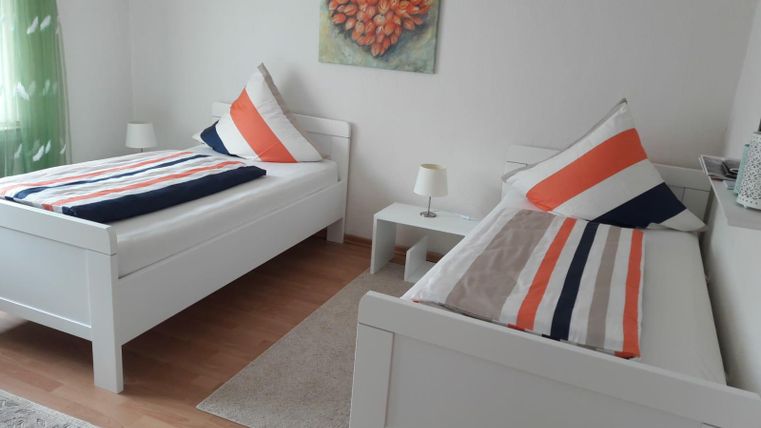 Een gezellige slaapkamer met twee eenpersoonsbedden en kleurrijke kussens. Aan de muur hangt een kunstwerk in de vorm van een hart.