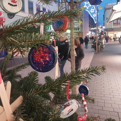 A decorated Christmas tree with colorful ornaments. In the background, people can be seen on a festively lit street.