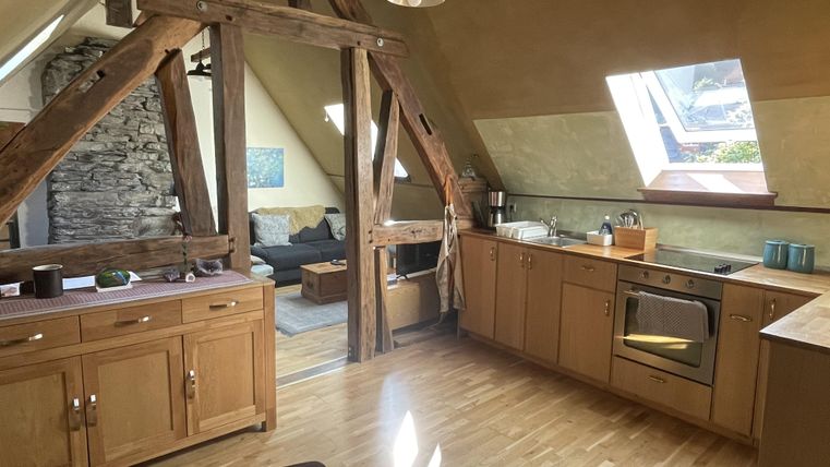 Eine gemütliche Küche mit Holzmöbeln und modernem Design. Im Hintergrund ist ein Wohnbereich mit einem gemütlichen Sofa zu sehen.