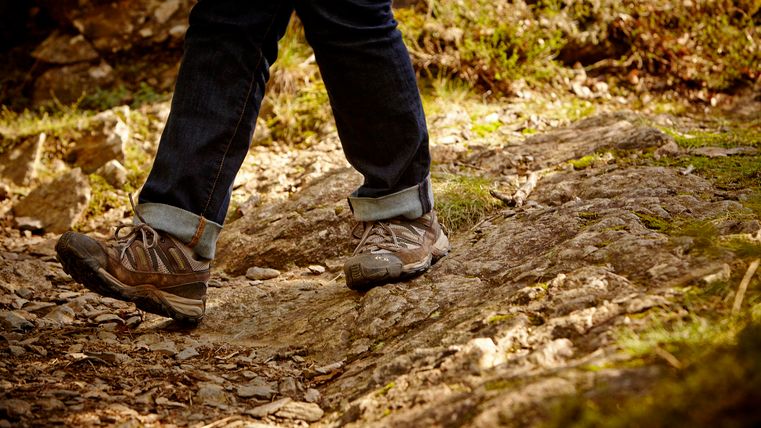 A person is hiking along an uneven, rocky path. The shoes are suitable for the terrain.