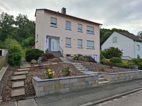 A modern house with a well-maintained garden layout. The entrance is lined with a path of stones and colorful flowers.