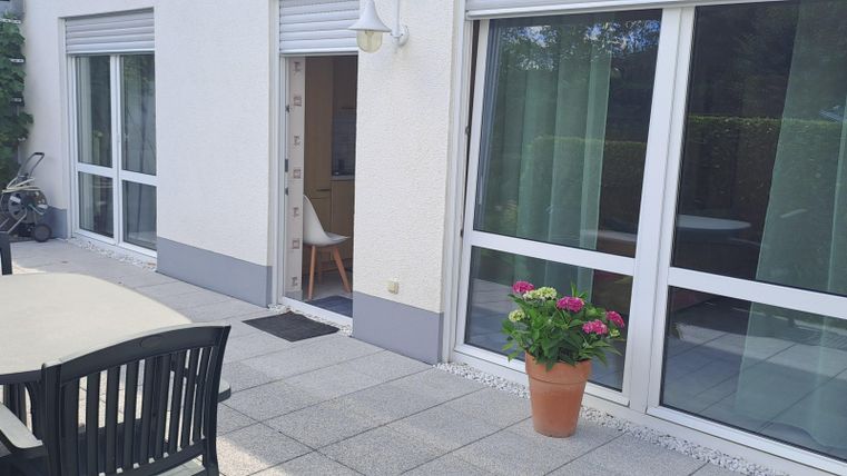 Een mooie buitenruimte met een tafel en stoelen. Vensters met gordijnen en enkele planten zorgen voor een uitnodigende sfeer.