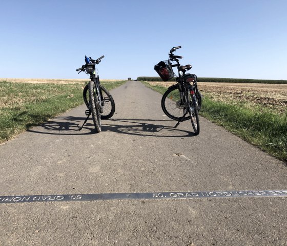 Zwei Fahrräder stehen auf einem ländlichen Weg, der den 50. Breitengrad markiert. Der Himmel ist klar und blau., © Tourist Information Bitburger Land