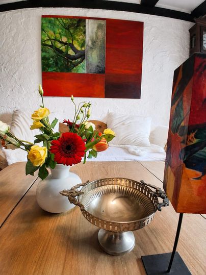 An elegant table with a silver bowl and a flower vase full of colorful flowers. In the background, a modern painting with vivid colors hangs.