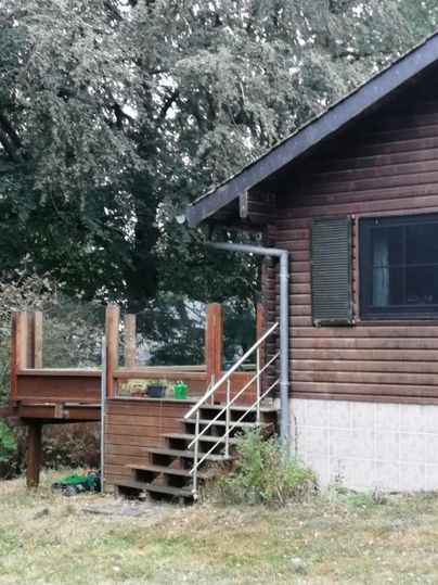 Een houten huis met een trap en een klein terras. Op de achtergrond zijn bomen zichtbaar.