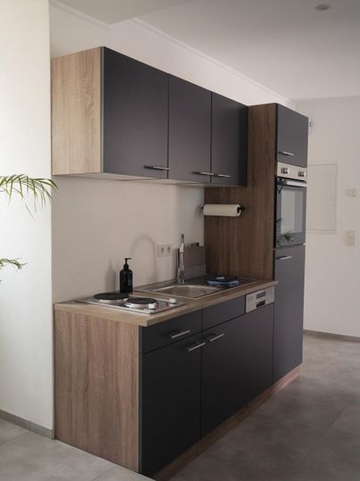 Een moderne keukenopstelling met zwarte en houtkleurige fronten. De uitrusting omvat een fornuis, een gootsteen en een oven.