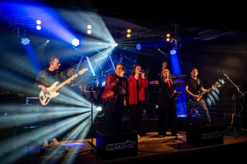 A band performs live on a stage. Colorful lights shine and the musicians create an energetic atmosphere.
