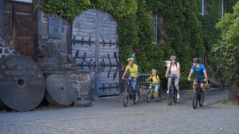 Une famille passe à vélo devant un vieux bâtiment couvert de lierre et une statue de lion.