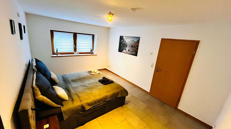 Een gezellig slaapkamer met een tweepersoonsbed en een houten vloer. De muren zijn licht en er zijn ramen die natuurlijk licht binnenlaten.
