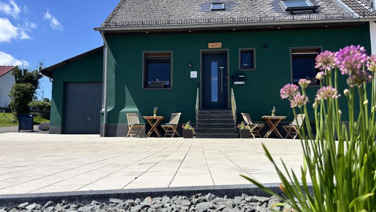Buitenaanzicht van het café en de pension Hamony Holiday met donkergroene muurverf vanuit de kikkerperspectief met bloemen op de voorgrond.