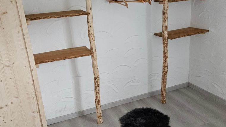 A minimalist room with a wooden shelf and a clothes rack. A black carpet lies on the floor.
