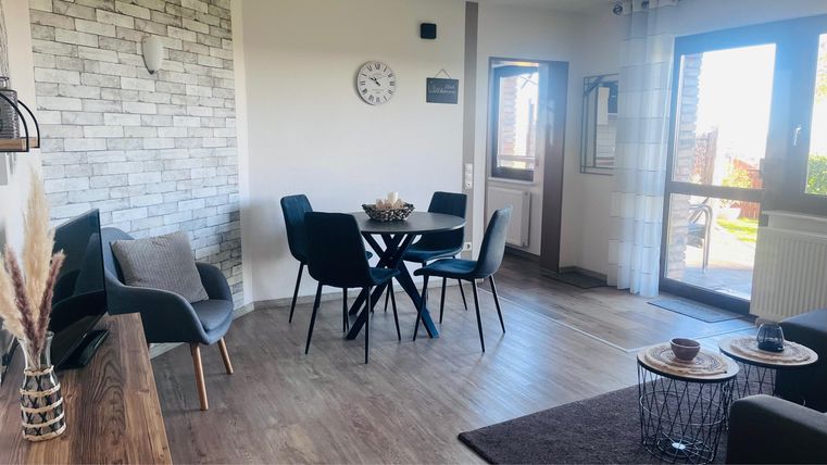 Ein helles und modernes Wohnzimmer mit einem Esstisch und Stühlen. Große Fenster sorgen für viel Tageslicht und eine einladende Atmosphäre.