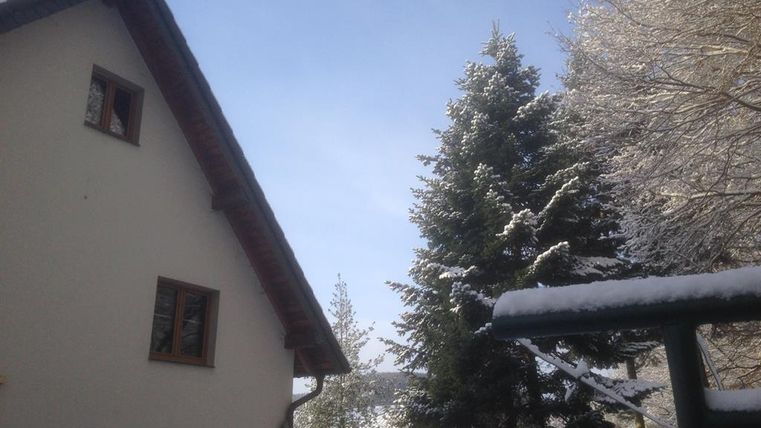 A snow-covered house with a clear blue sky and snow-covered trees. The scenery radiates tranquility and winter coziness.