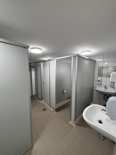 Une toilette moderne avec plusieurs cabines et lavabos. La pièce est bien éclairée et propre.