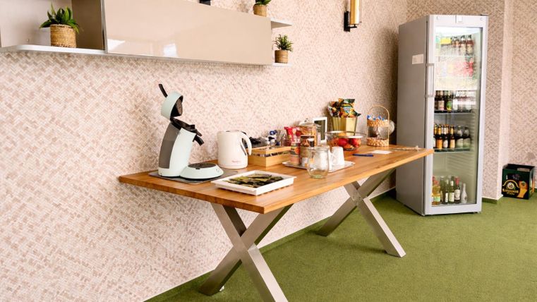 Eine moderne Kaffeebar mit einem Holz-Tisch und verschiedenen Getränken. Im Hintergrund steht ein Kühlschrank und die Wände sind dekoriert.