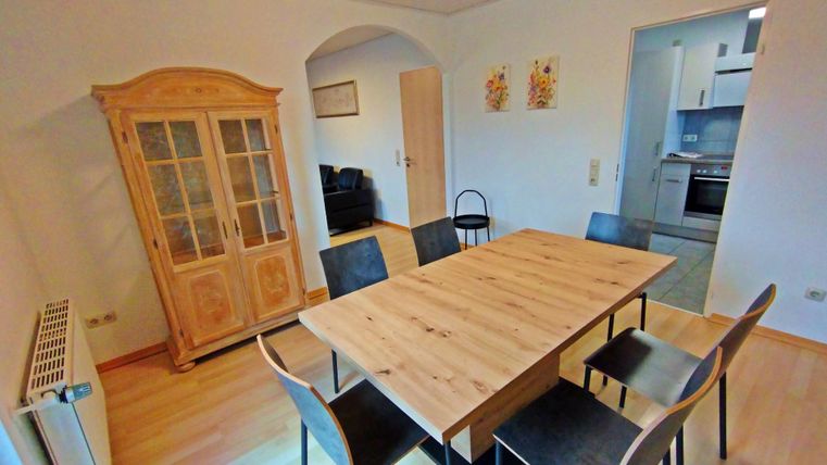 Un coin repas confortable avec une grande table en bois et des chaises noires. À l'arrière-plan, un joli buffet vitrine et une cuisine sont visibles.