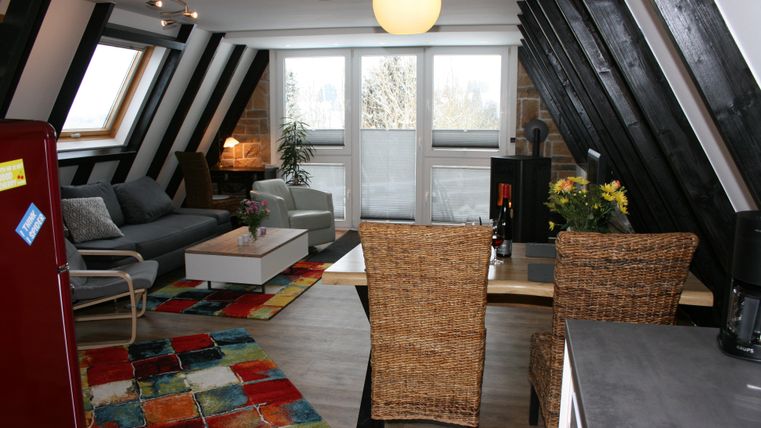 Un appartement confortable sous les combles avec vue sur le salon et la salle à manger. Les poutres en bois et le tapis coloré donnent à la pièce un charme moderne.