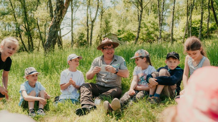 <p>Ranger sitzt mit Kindern im Gras </p>