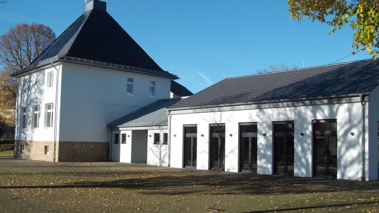 Gemeindehaus Messerich mit blauem Himmel und Herbstlaub.